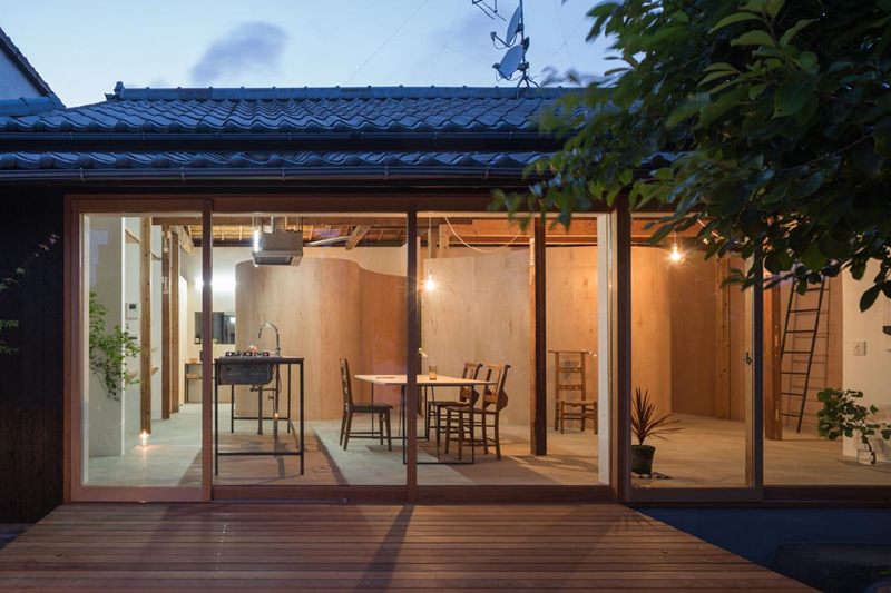 Fasad rumah panggung dengan panel geser kayu, dikelilingi taman bergaya Jepang.