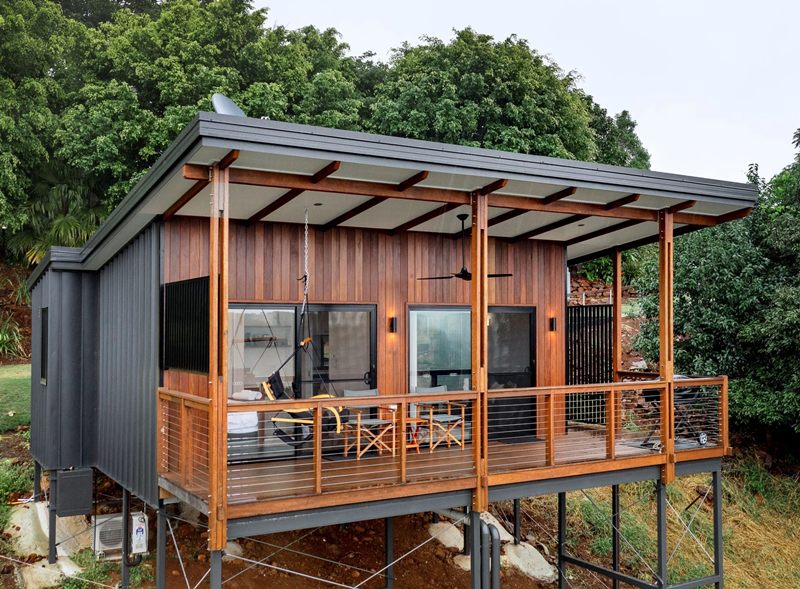 Rumah panggung bertingkat dengan balkon kayu, tangga luar, dan fasad bergaya Jepang.